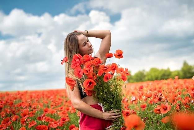 Jovem ucraniana feliz segurando um buquê de flores de papoula, caminhando e aproveitando o dia de sol no campo