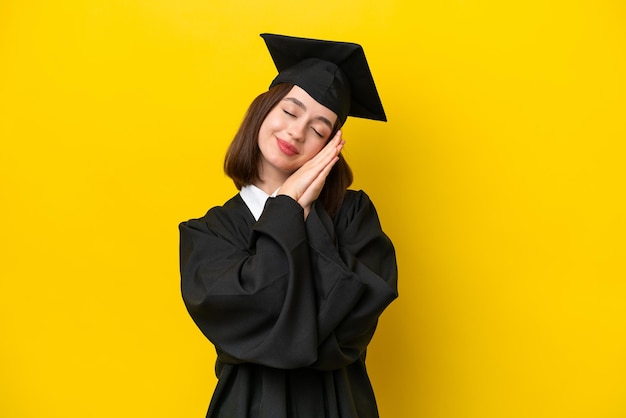 Jovem ucraniana graduada em universidade isolada em fundo amarelo fazendo gesto de sono em expressão dorável