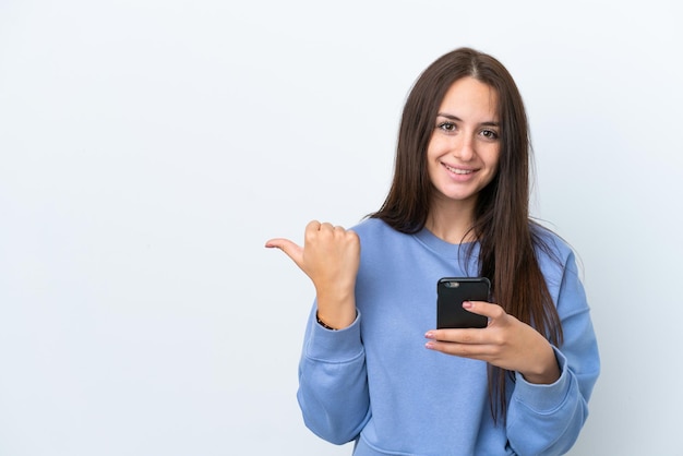 Jovem ucraniana isolada em fundo branco usando telefone celular e apontando para a lateral