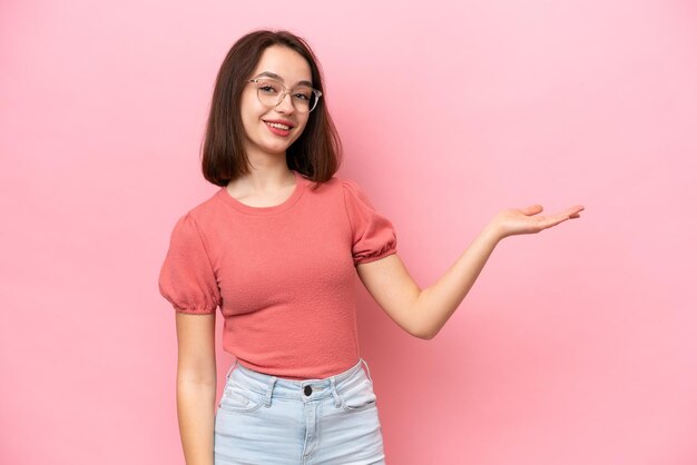 Foto jovem ucraniana isolada em fundo rosa, estendendo as mãos para o lado para convidar para vir