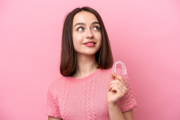 Jovem ucraniana segurando aparelhos invisíveis isolados em fundo rosa olhando para cima enquanto sorria