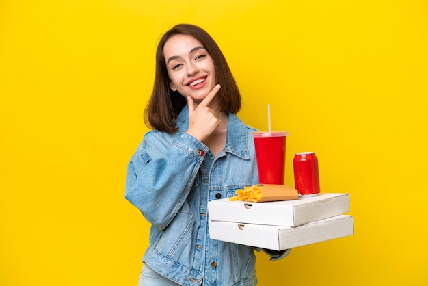 Jovem ucraniana segurando fast food isolada em fundo amarelo feliz e sorridente