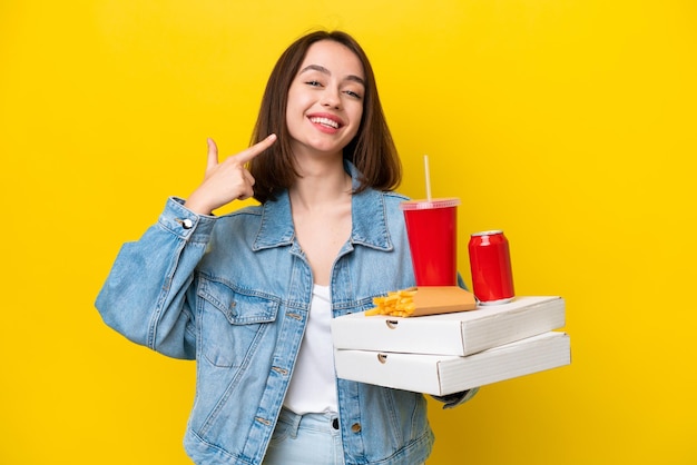 Jovem ucraniana segurando fast food isolado em fundo amarelo dando um polegar para cima gesto