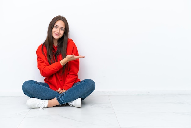 Jovem ucraniana sentada no chão isolada em fundo branco apresentando uma ideia enquanto olhava sorrindo para