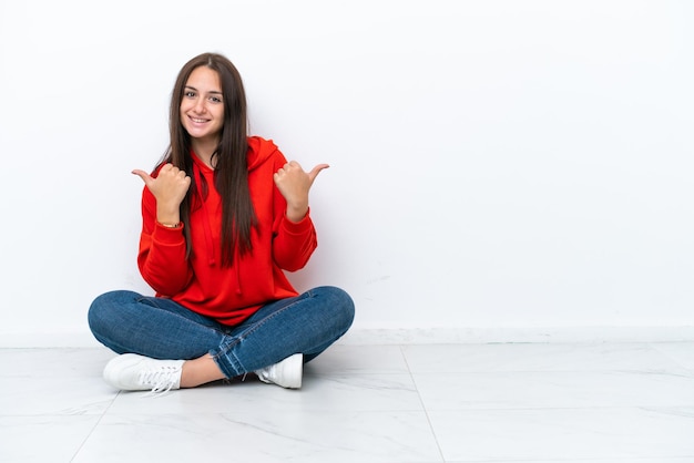 Jovem ucraniana sentada no chão isolada em fundo branco com polegares para cima gesto e sorrindo