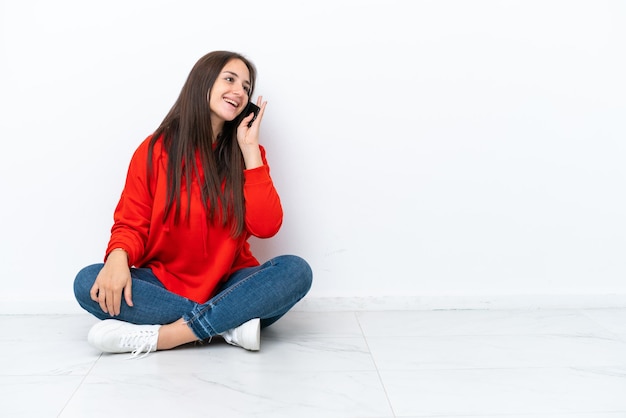 Jovem ucraniana sentada no chão isolada em fundo branco mantendo uma conversa com o celular