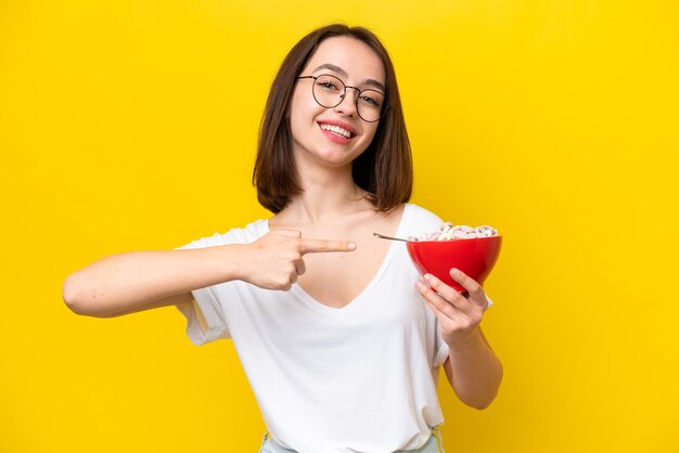 Jovem ucraniano segurando uma tigela de cereais isolado de fundo amarelo e apontando-o