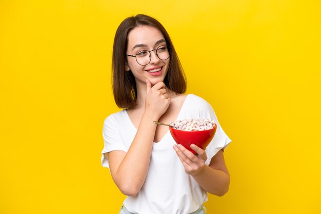 Jovem ucraniano segurando uma tigela de cereais isolado de fundo amarelo pensando em uma ideia e olhando de lado