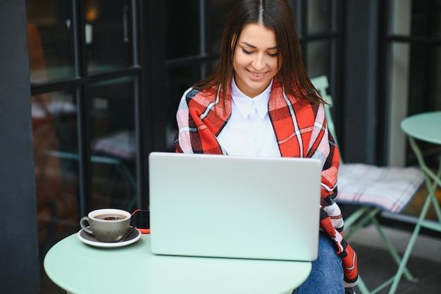 Jovem, uma garota em um café ao ar livre com um laptop conversando por meio de uma videochamada com alguém, telefonia aipi