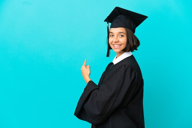 Jovem universitária sobre fundo azul isolado apontando para trás