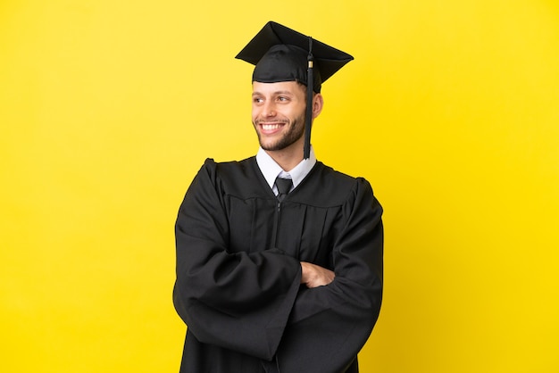 Jovem universitário, homem branco, isolado em um fundo amarelo, feliz e sorridente.