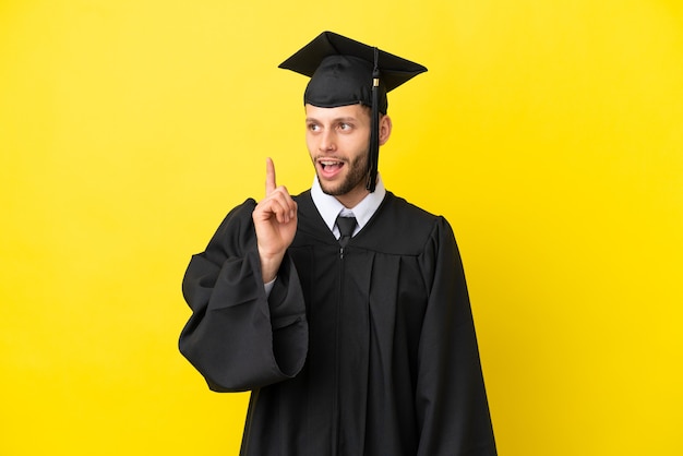 Jovem universitário, homem branco, isolado em um fundo amarelo, pensando em uma ideia apontando o dedo para cima