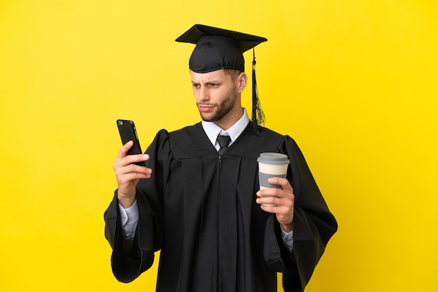 Jovem universitário, homem branco, isolado em um fundo amarelo, segurando um café para levar e um celular