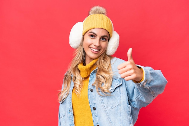 Jovem uruguaia bonita vestindo regalos de inverno isolados em fundo vermelho com polegares para cima porque algo bom aconteceu