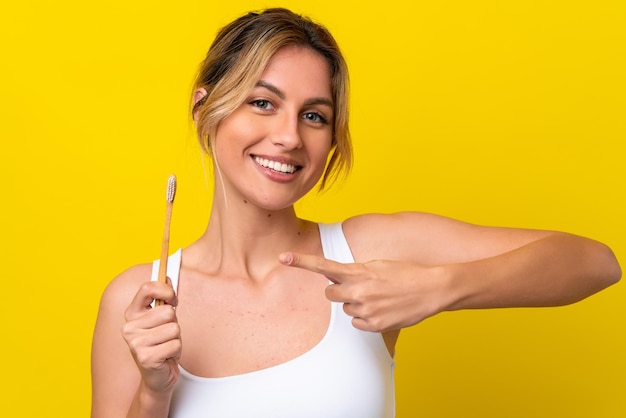 Jovem uruguaia escovando os dentes isolados em fundo amarelo e apontando-o