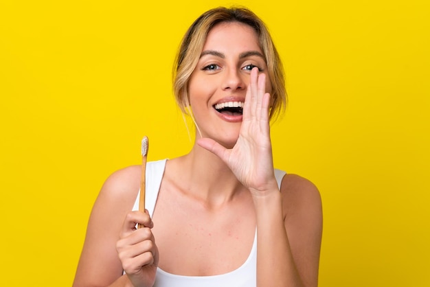 Foto jovem uruguaia escovando os dentes isolados em fundo amarelo gritando com a boca aberta