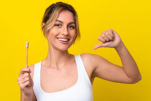 Jovem uruguaia escovando os dentes isolados em fundo amarelo orgulhoso e satisfeito