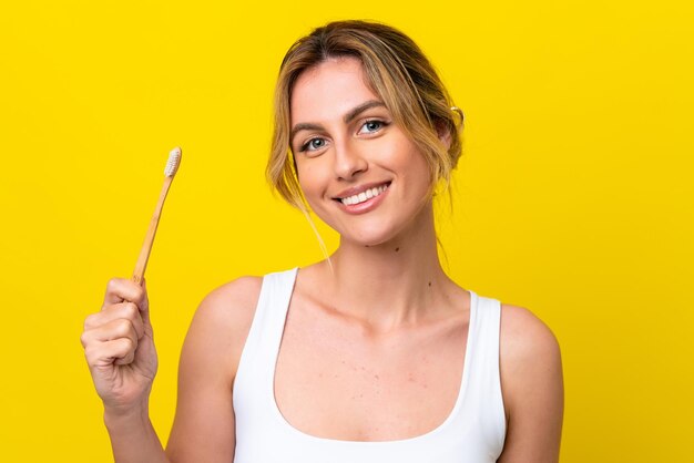 Jovem uruguaia escovando os dentes isolados no fundo amarelo sorrindo muito