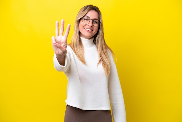 Jovem uruguaia isolada em fundo amarelo feliz e contando três com os dedos