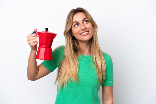 Jovem uruguaia segurando a cafeteira isolada no fundo branco olhando para cima enquanto sorria