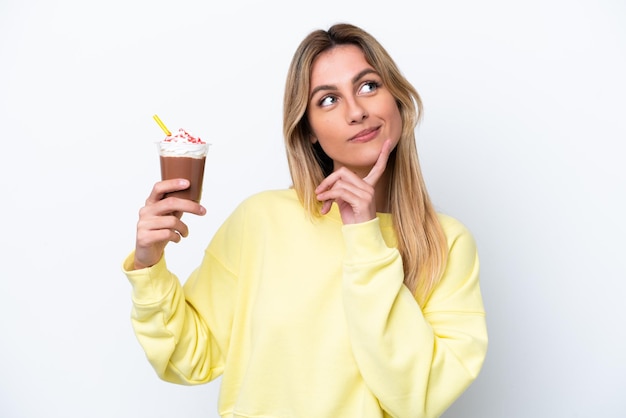 Jovem uruguaia segurando Frappuccino isolado no fundo branco pensando em uma ideia enquanto olha para cima