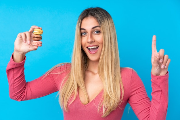 Jovem uruguaia segurando macarons franceses coloridos e apontando uma ótima idéia