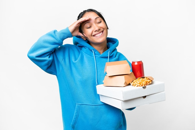 Jovem uruguaia segurando pizzas e hambúrgueres sobre fundo branco isolado sorrindo muito