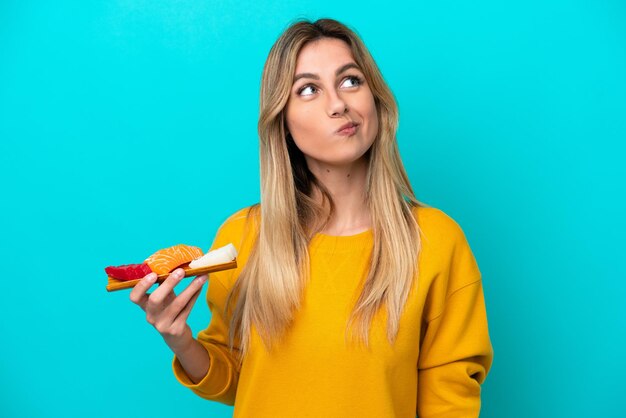 Foto jovem uruguaia segurando sashimi isolado em fundo azul e olhando para cima