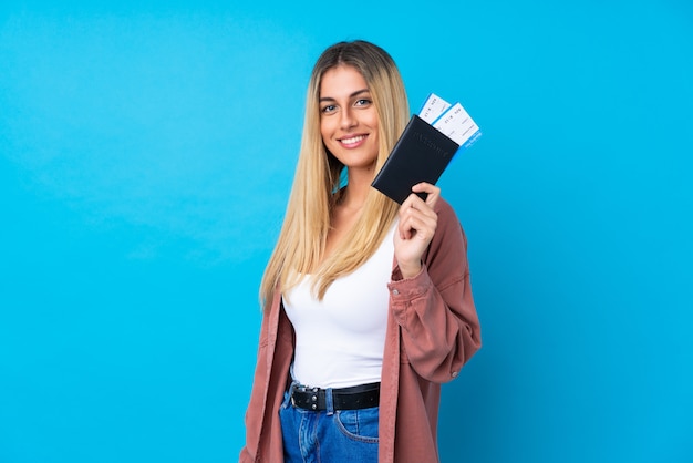 Foto jovem uruguaia sobre parede azul isolada feliz em férias com bilhetes de avião e passaporte