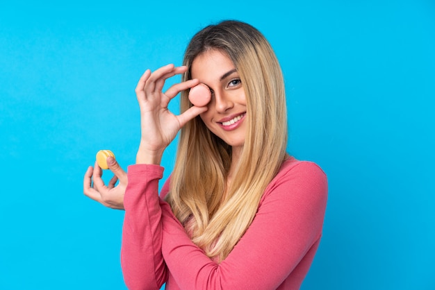 Jovem uruguaia sobre parede isolada parede azul segurando macarons franceses coloridos