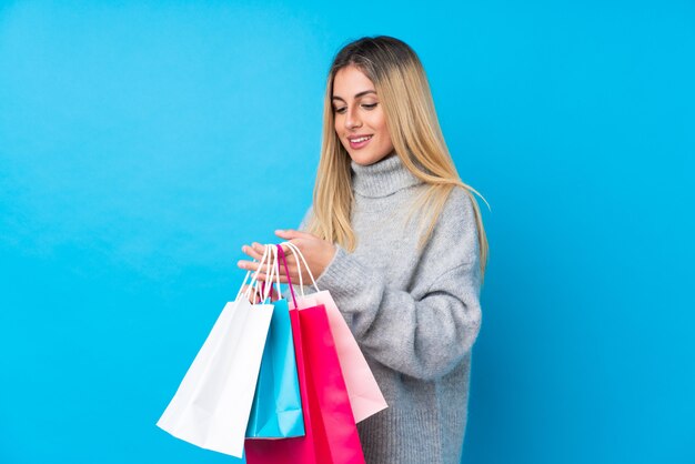 Jovem uruguaia sobre parede isolada parede azul segurando sacolas de compras