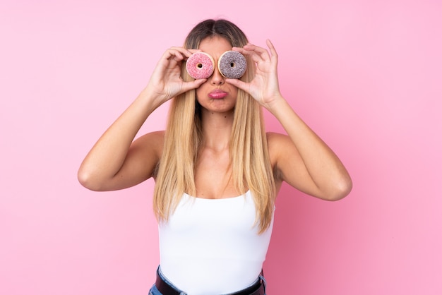 Jovem uruguaia sobre parede rosa isolada segurando rosquinhas nos olhos com expressão triste