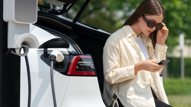 Foto jovem usa smartphone para pagar eletricidade na estação pública de carregamento de carros ev parque verde da cidade estilo de vida urbano ambiental e sustentável moderno com veículo ev expediente