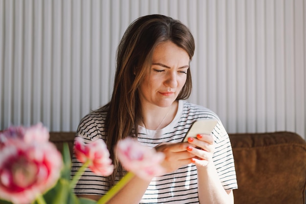 Jovem usa telefone celular Beba café e sente-se sozinha à mesa na cafeteria