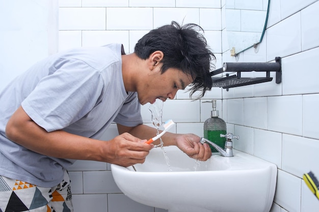 Jovem usando água para limpar os dentes e a boca após escovar os dentes Higiene matinal