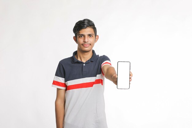 Jovem usando fone de ouvido e mostrando o smartphone em fundo branco.