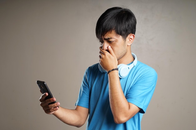 Jovem usando fones de ouvido no pescoço e segurando um smartphone com uma expressão de espanto