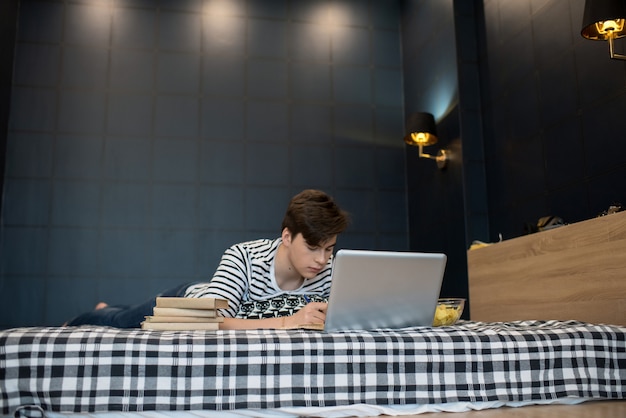 Jovem usando laptop e escrevendo na cama