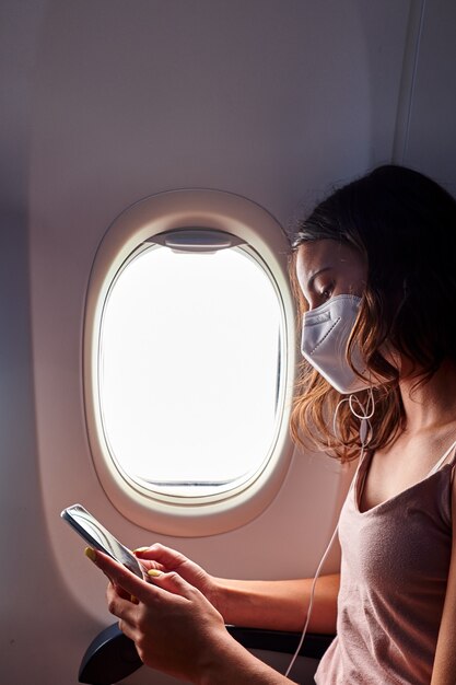 Foto jovem usando máscara facial usando smartphone enquanto viaja de avião