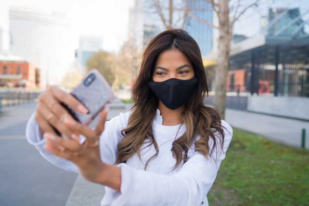 jovem usando máscara protetora e tirando selfies com seu telefone mophile ao ar livre. Conceito urbano.