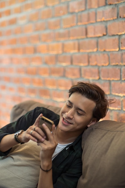 Jovem usando o telefone junto à parede de tijolos no sofá