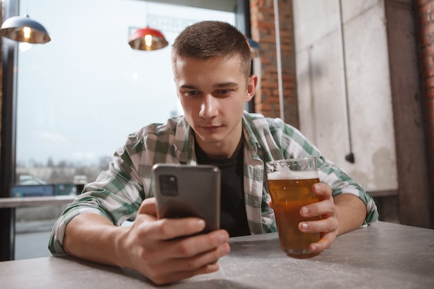 Jovem usando seu smartphone enquanto bebe cerveja no bar