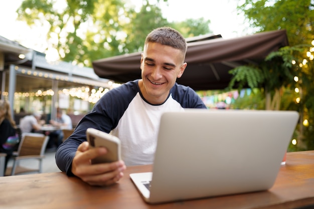 Jovem usando smartphone enquanto está sentado em um café ao ar livre