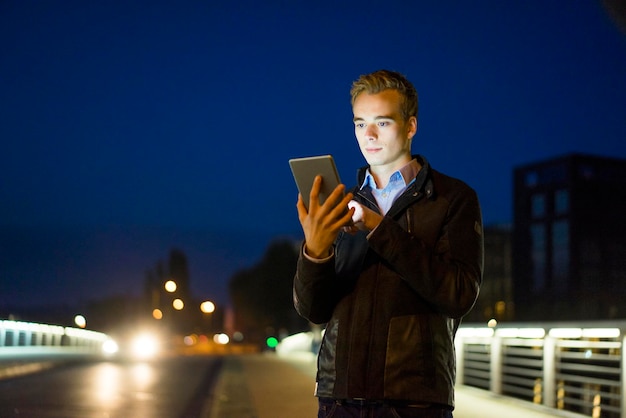 Jovem usando tablet qutdoors à noite