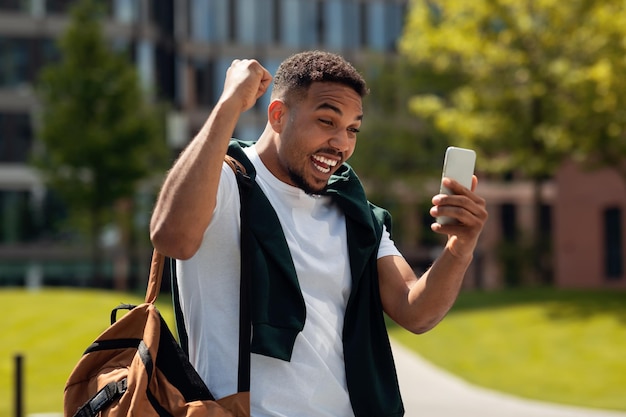 Jovem usando telefone celular comemorando sucesso agitando os punhos