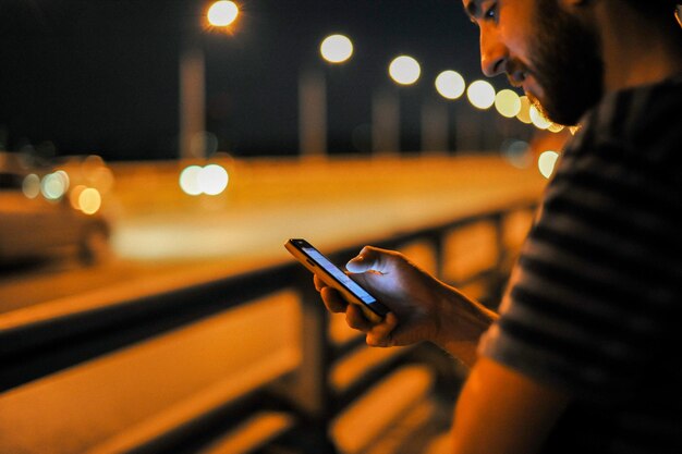 Foto jovem usando telefone celular na ponte à noite