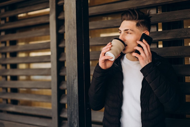 Jovem usando telefone e tomando café na rua