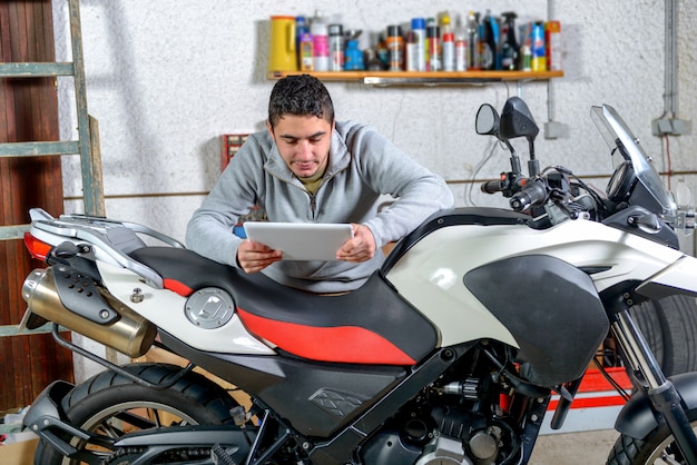 Jovem usando um tablet ao lado de motocicleta