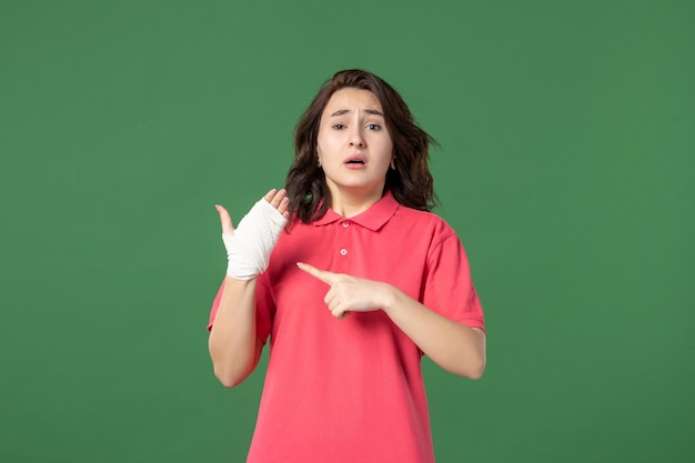 Jovem vendedora com bandagem na mão machucada de frente no fundo verde cor do trabalho uniforme lesão saúde hospital compras trabalho