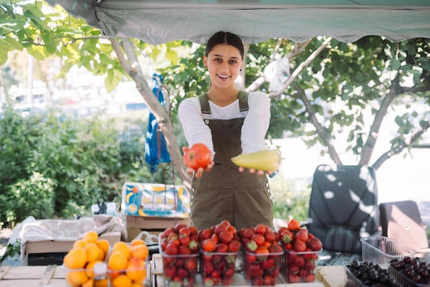 Jovem vendedora segurando pimentão e tomate nas mãos